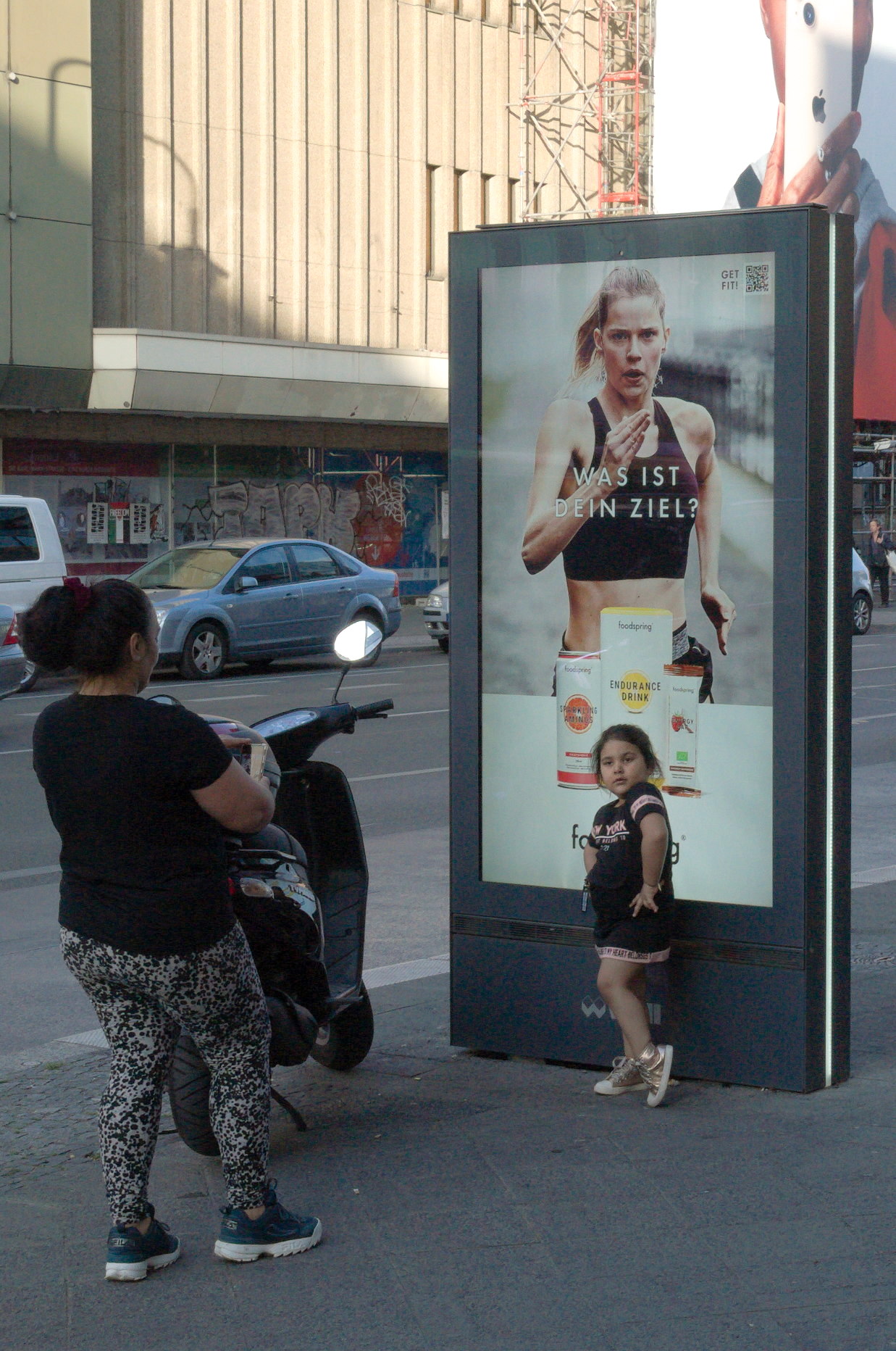 La niña posa para una foto delante del cartel publicitario. 'el soporte', documentalismo subjetivo en Berlín-Neukölln. Obra de la serie 'el soporte' por Ibán Ojea.