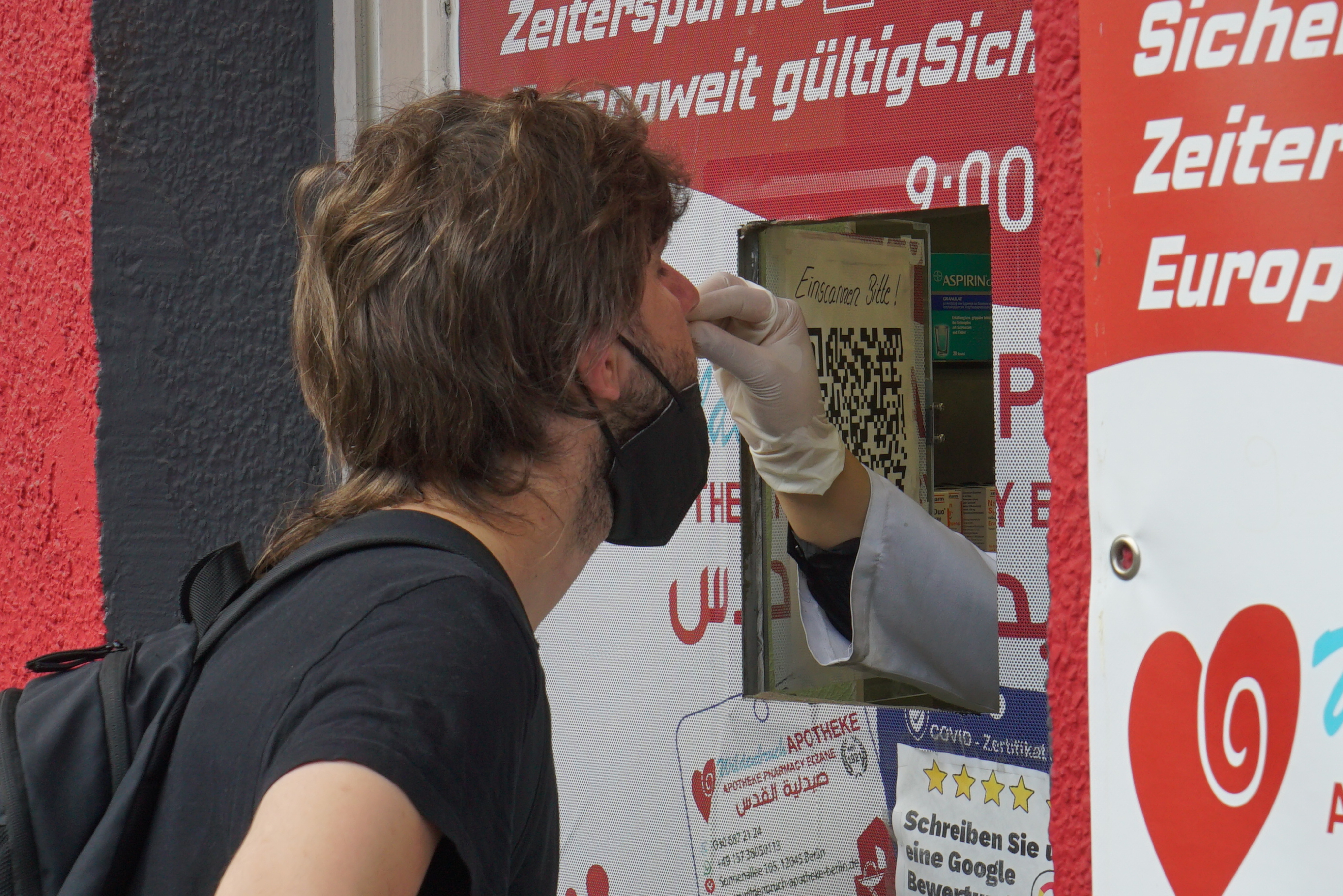 A través de la ventanita, ya abierta, aparece una mano que le introduce al muchacho un palito por la nariz para hacerle un test PCR. Ensayo fotográfico en Berlín. Obra de la serie 'el soporte' por Ibán Ojea.