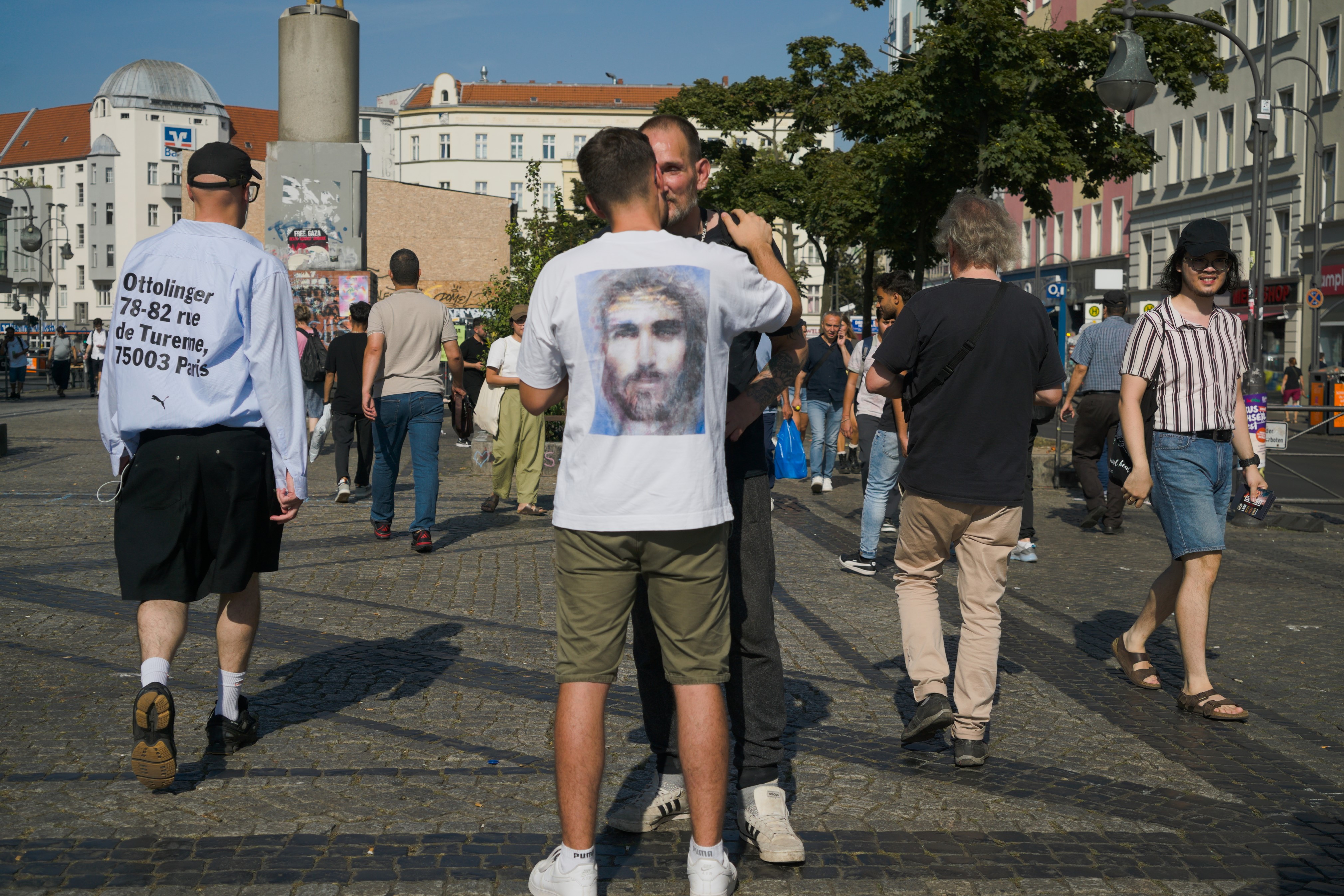 Nos mira un Cristo estampado en una camiseta que viste una persona que consuela a otra. Serie 'el soporte', fotografía de Ibán Ojea en Berlín.