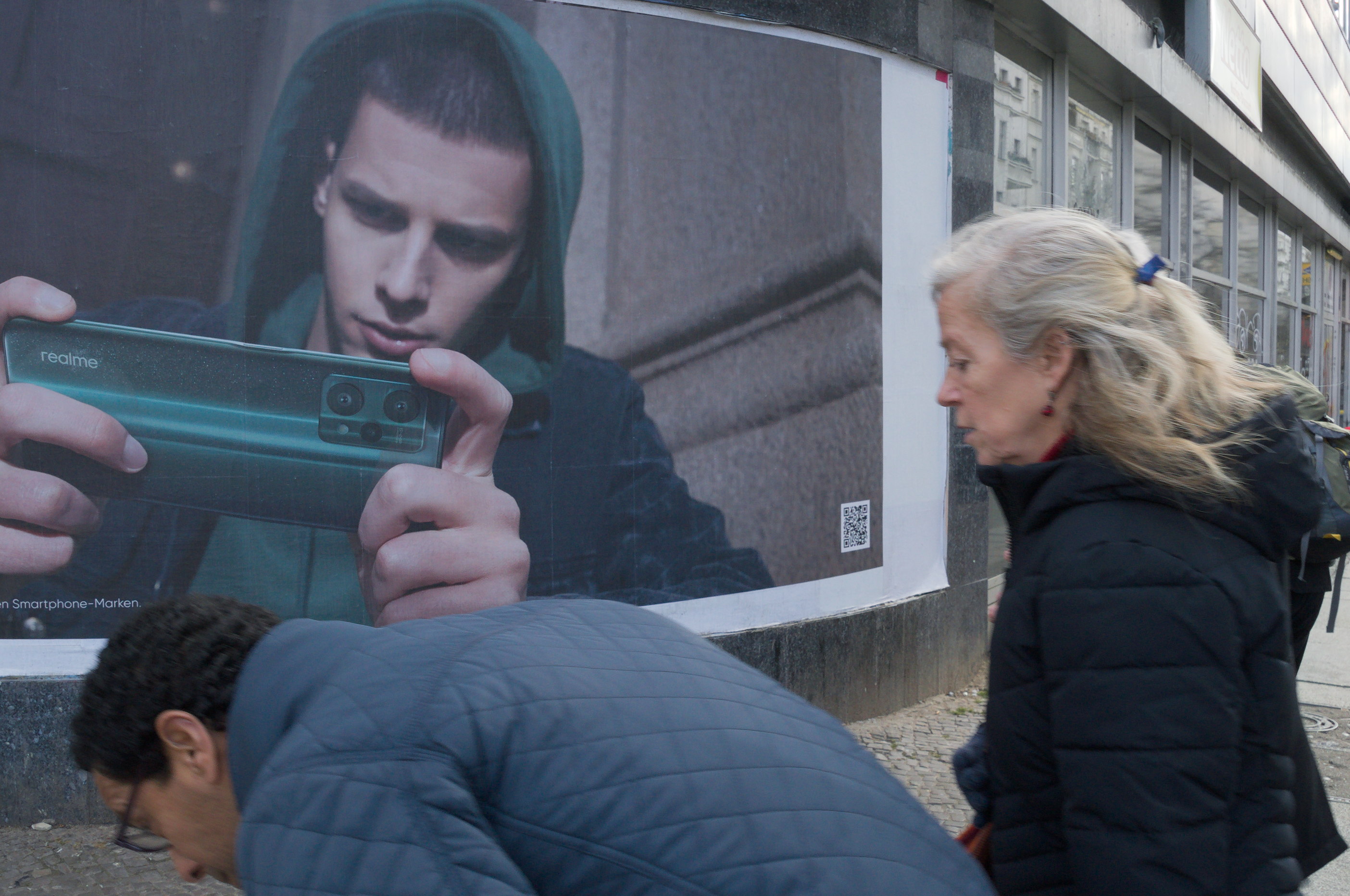 Un hombre se agacha para no interponerse entre el fotógrafo y un cartel que muestra a alguien fotografiando. Berlín. De la serie 'el soporte' por Ibán Ojea.