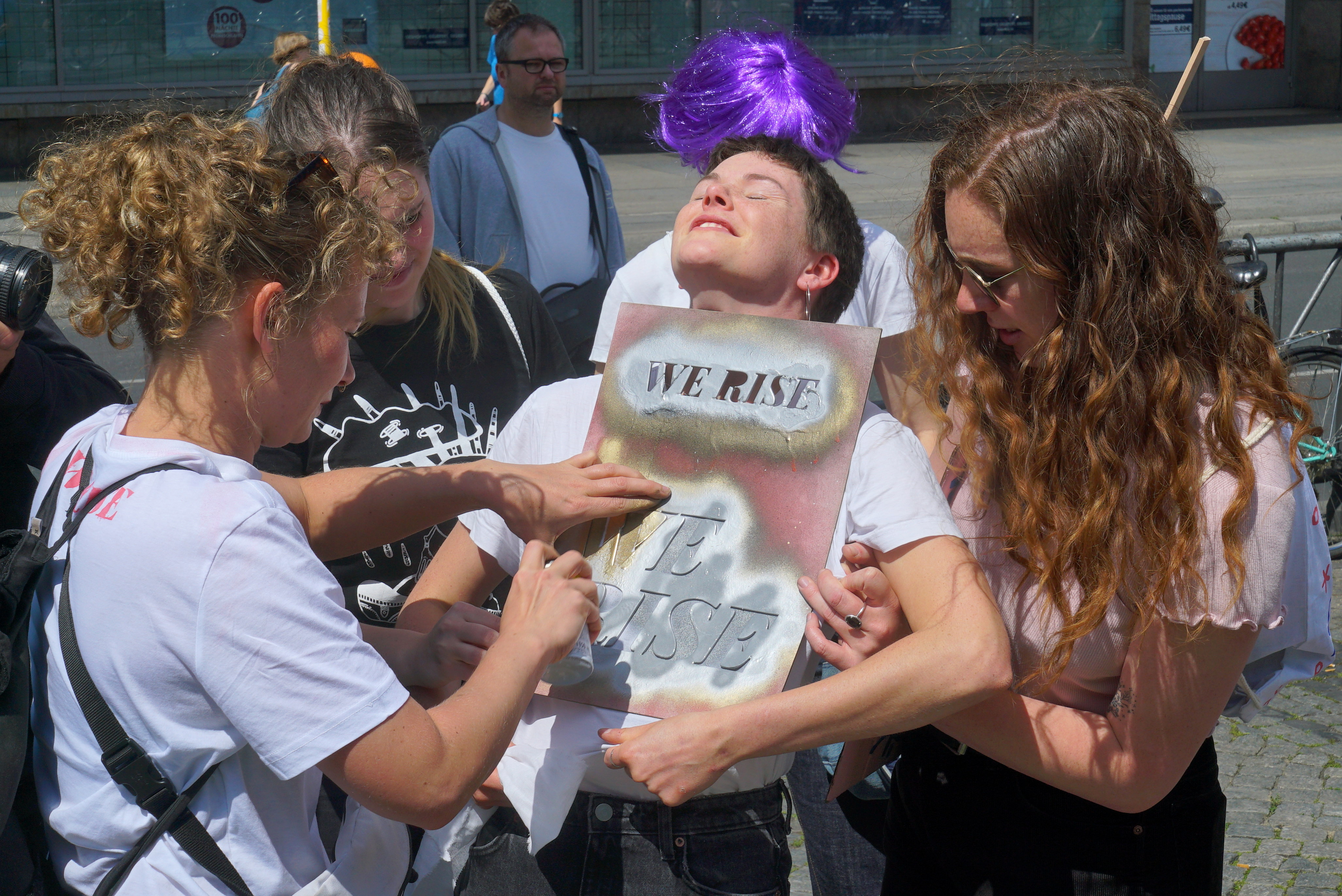 Unas chicas pintan 'We rise' sobre la camiseta de una tercera chica. Serie 'el soporte' por Ibán Ojea.