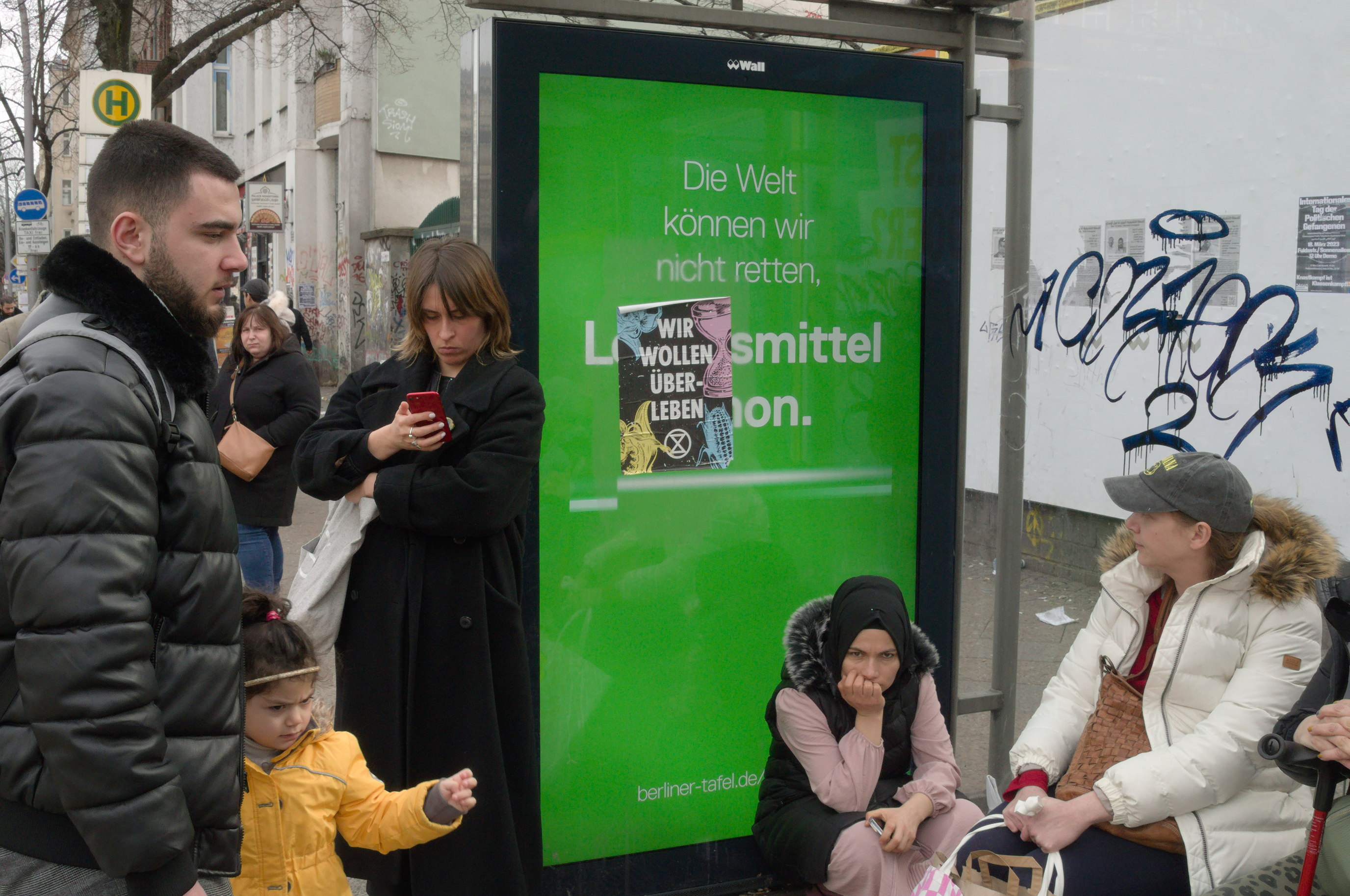 En una pantalla publicitaria donde vemos el mensaje 'Die Welt können wir nicht retten' hay una cartel pegado con las palabras 'Wir wollen überleben'. Serie 'el soporte', fotografía de Ibán Ojea en Berlín.